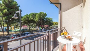 Un balcon avec une table et des chaises, donnant sur une rue bordée d’arbres et où circulent des voitures.