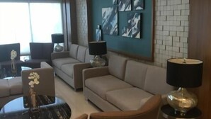 Un salon moderne avec un canapé, des fauteuils et une table basse. Un climatiseur mural est fixé au mur, et une œuvre d’art abstraite y est également accrochée.