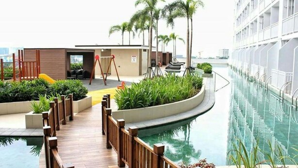 Un espace piscine doté d’une terrasse en bois, de palmiers et d’un bâtiment avec des balcons.