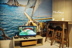 A room with a television displaying a show, a wooden table with chairs, and a mural of a sailboat on the wall. - MaxStays Max View at Breeze Residences (Pasay)