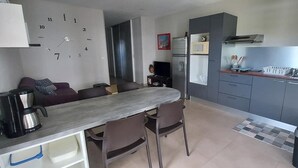 A compact kitchen with a dining area, a microwave, a refrigerator, and a clock on the wall. - Rangiroa Tiputa Lodge B&B (Rangiroa)