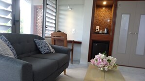A living room with a grey sofa, patterned cushions, a wooden side table, and a vase of flowers. - Rangiroa Tiputa Lodge B&B (Rangiroa)