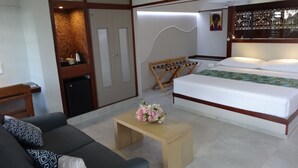 A modern hotel room with a bed, a sofa, a small table with flowers, a wardrobe, and a desk. - Rangiroa Tiputa Lodge B&B (Rangiroa)