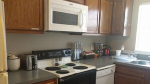 A kitchen with wooden cabinets, a microwave, stove, toaster, and dishwasher. - The Better Half Duplex on 7th (Charlotte)