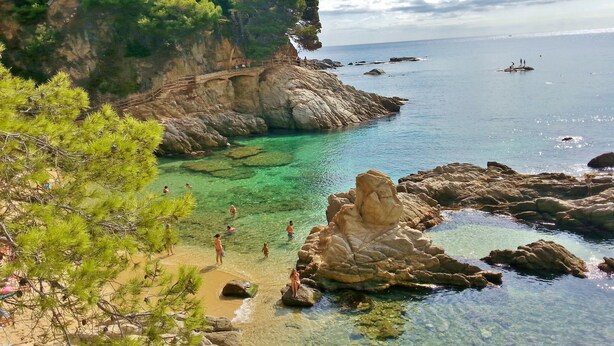 A coastal area with clear waters, rocky terrain, and a bridge connecting the cliffs to the beach.