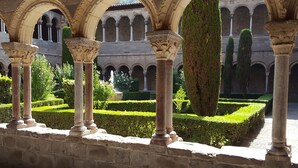 A courtyard with stone columns, a fountain, and neatly trimmed hedges.