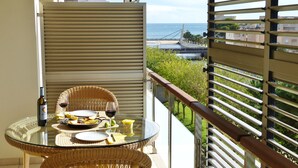 A balcony with a glass table set for dining, featuring a bottle of wine, a glass, and a plate of food.