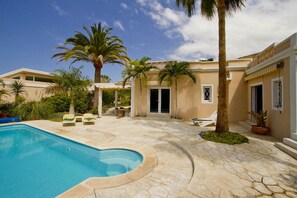 A pool area with lounge chairs, palm trees, and a building with a door and windows. - Villa Tauro, detached with solar / electric heated pool and garden (Tauro)