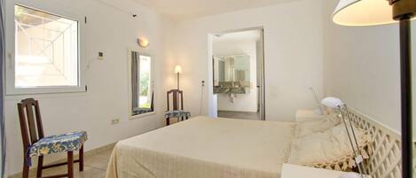 Un dormitorio con cama, una silla, una lámpara y una ventana.