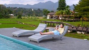 Two lounge chairs by a swimming pool with a view of a mountainous landscape and a traditional building in the background.
