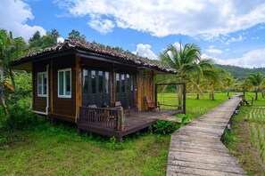 A wooden house with a porch, surrounded by lush greenery and palm trees.