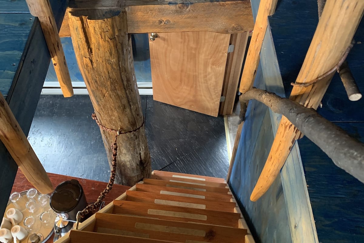 A wooden staircase with a rustic design, leading to a room with a blue wall and a window.
