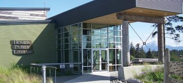 The exterior of Homer Public Library with a modern glass facade and a covered entrance.