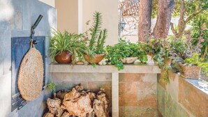 Un estante de piedra con diversas plantas en macetas, un bolso tejido colgante y una pila de leña.