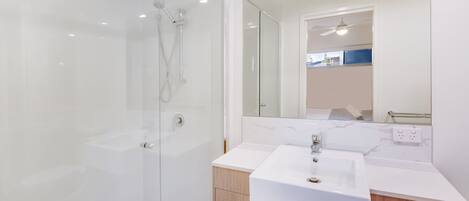 Ein modernes Badezimmer mit einer gläsernen Duschkabine, einem weißen Waschbecken und Holzschränken.