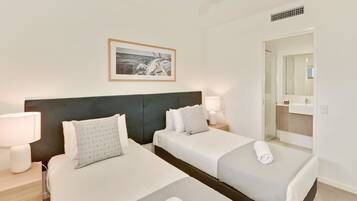 A hotel room with two beds, a large mirror, a framed picture on the wall, and a bathroom visible through an open door.