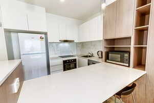 A modern kitchen with white cabinets, a marble backsplash, a built-in oven, a microwave, and a sink.