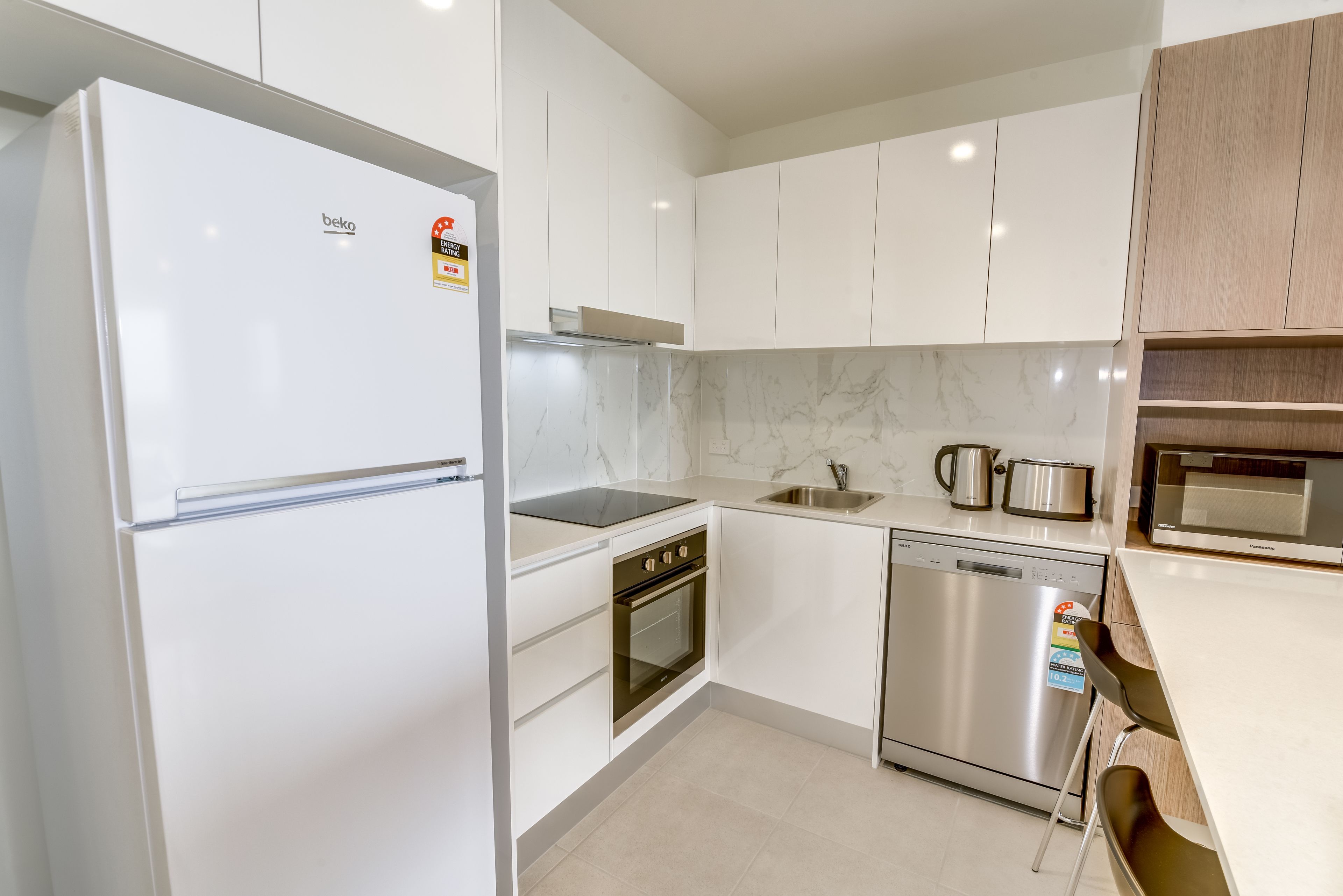 A modern kitchen with white cabinets, a stainless steel refrigerator, a built-in oven, a dishwasher, and a microwave.