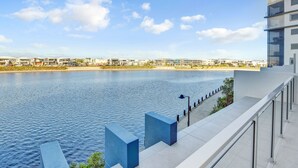 A waterfront view with modern buildings, a clear sky, and a calm body of water.