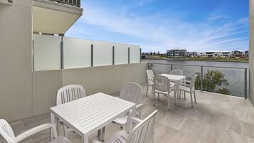 A balcony with a white table and chairs, a view of a river, and a cityscape in the background.