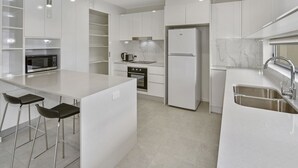 A modern kitchen with white cabinetry, a built-in oven, a stainless steel refrigerator, and a large island with bar stools.