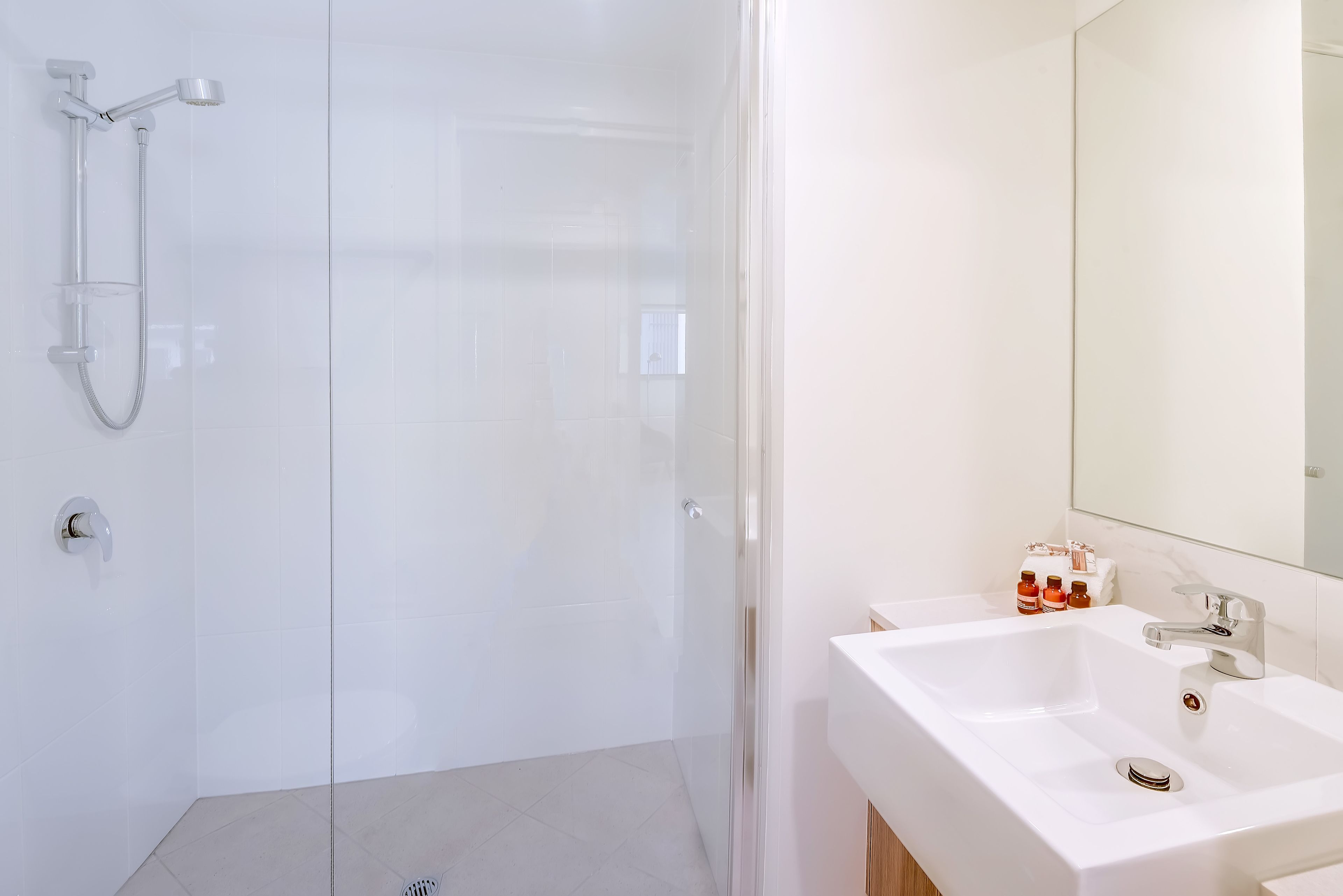 Un baño moderno con cabina de ducha de vidrio, un lavabo blanco con espejo y artículos de aseo en la encimera.