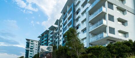 A modern multi-story hotel with balconies, a waterfront view, and a paved walkway.