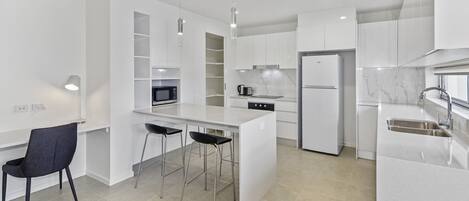 Una cocina moderna con armarios blancos, una isla central con taburetes y un microondas integrado, además de un refrigerador de acero inoxidable.