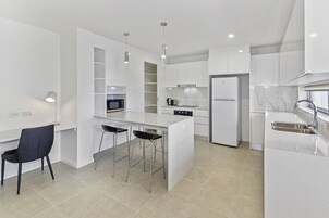 A modern kitchen with white cabinetry, a central island with bar stools, a built-in microwave, and a stainless steel refrigerator.