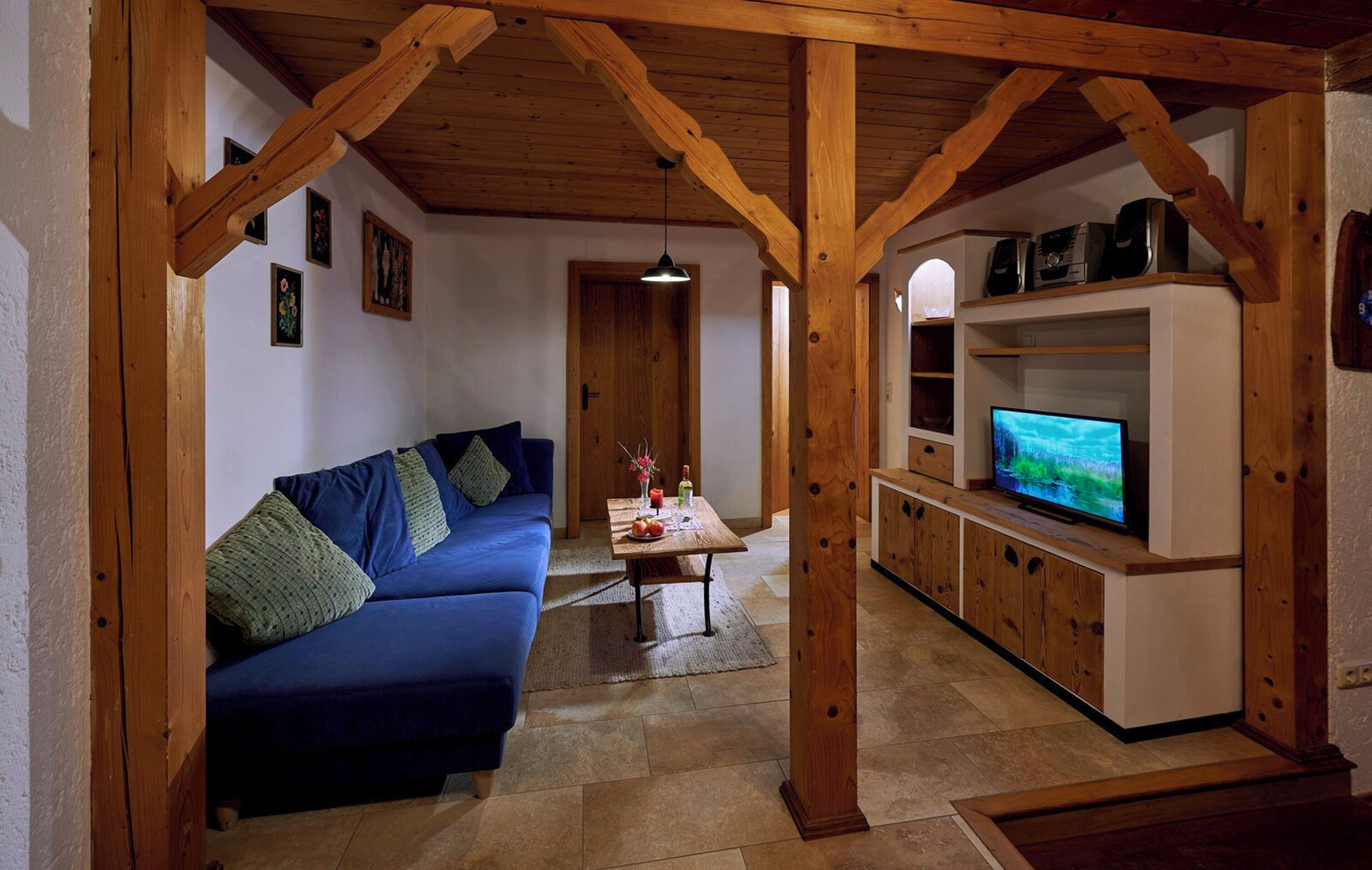 Una sala de estar acogedora con un sofá azul, vigas de madera, un televisor y una mesita con adornos.