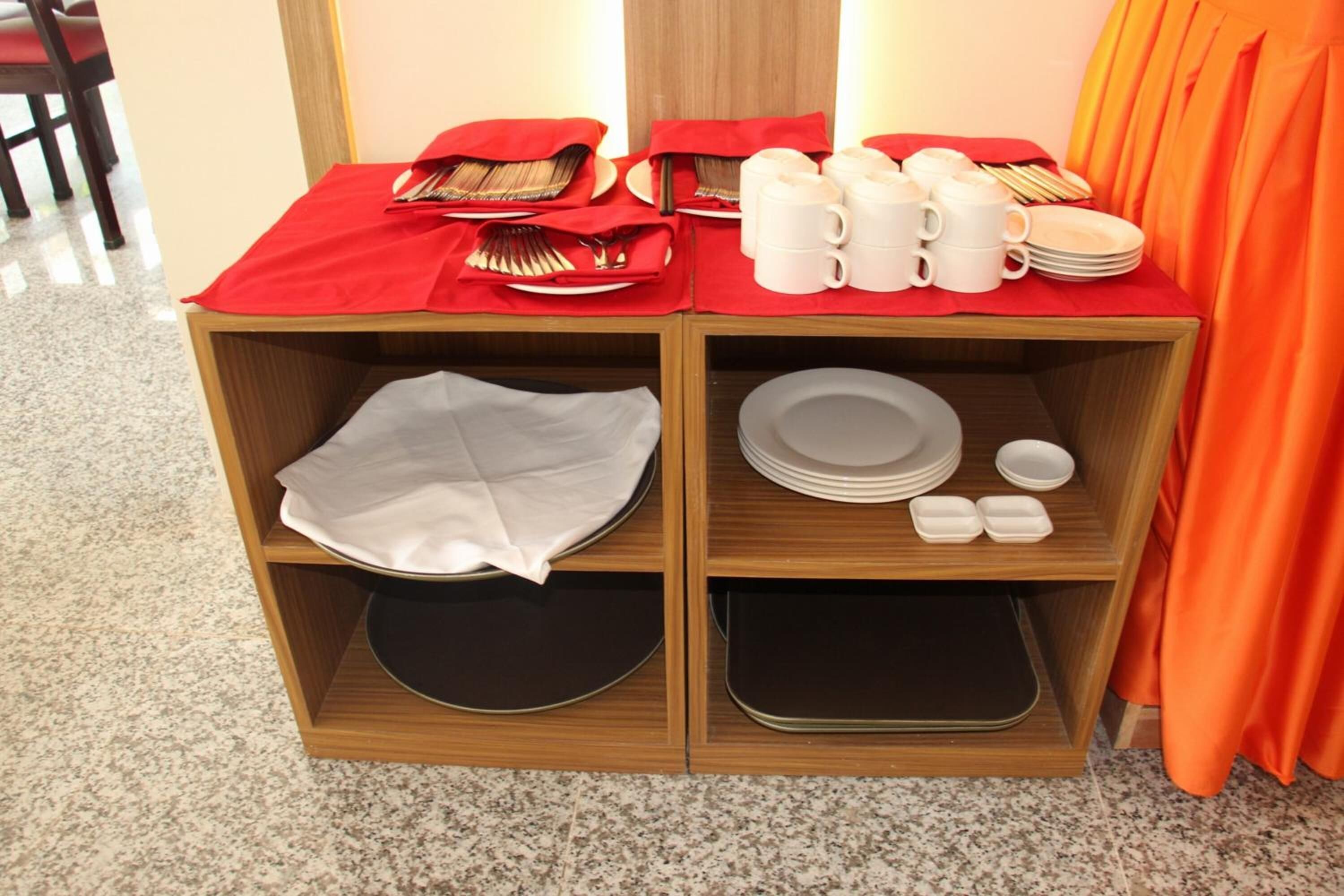A wooden buffet table with red tablecloths, white plates, bowls, and cups.