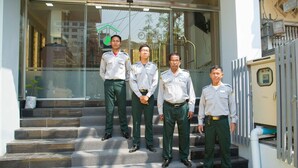 Four uniformed individuals standing on a staircase outside a building with glass doors and metal railings. - Orient Hotel (Mandalay)
