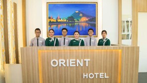 A reception desk at the Orient Hotel with a wooden finish and a cityscape painting above it. - Orient Hotel (Mandalay)