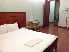 A bedroom with a large bed, a wooden headboard, a small table with chairs, and a coat rack. - TK 134 Hotel (Hanoi)