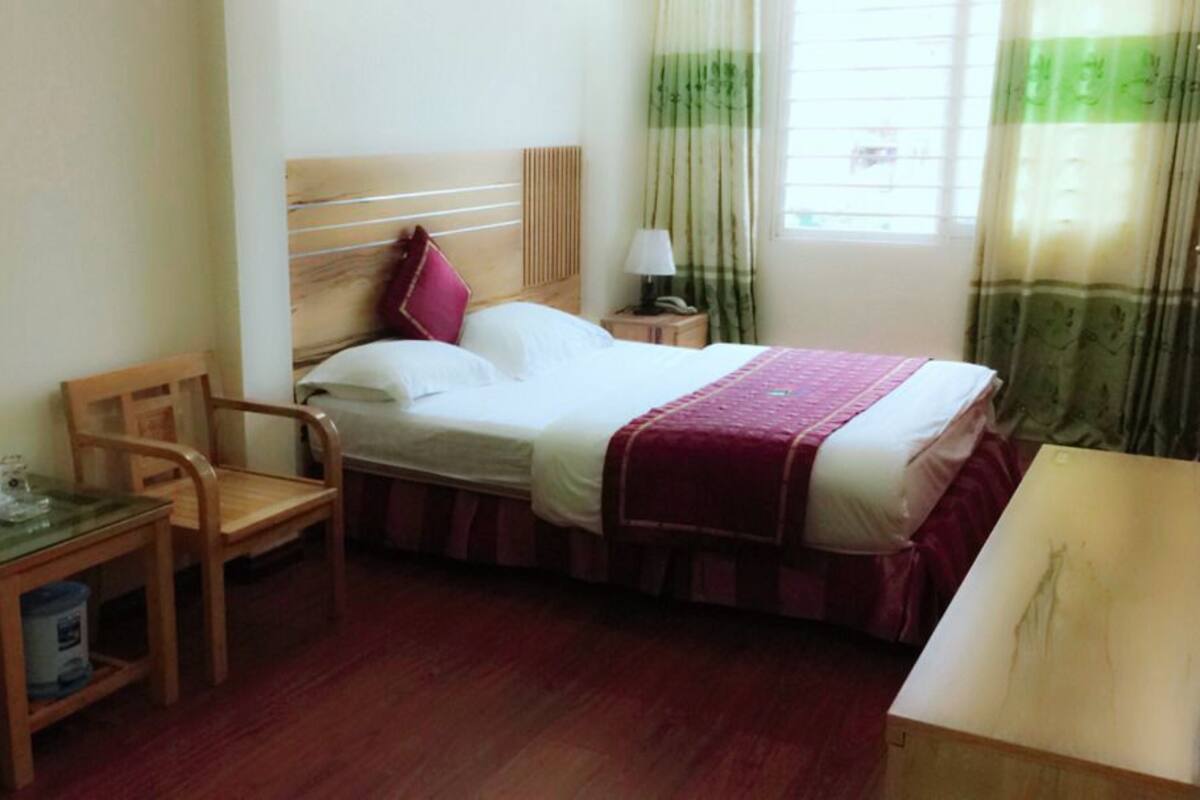 A hotel room with a bed, a desk, a chair, a nightstand, and a window with curtains.