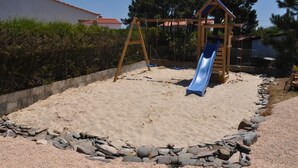 Un área de juegos con arena, un columpio de madera y un tobogán.