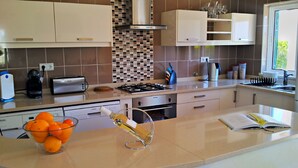 Una cocina moderna con una encimera curva, horno empotrado y estufa a gas. Hay armarios, una cafetera y un frutero en la encimera.