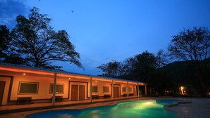 A poolside area with a swimming pool, a covered seating area, and a building with multiple windows and doors. - Suansaiyok Resort (Sai Yok)