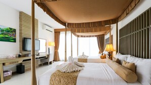 A hotel room with a large bed, a desk with a computer, a TV, and a painting on the wall. - Suansaiyok Resort (Sai Yok)