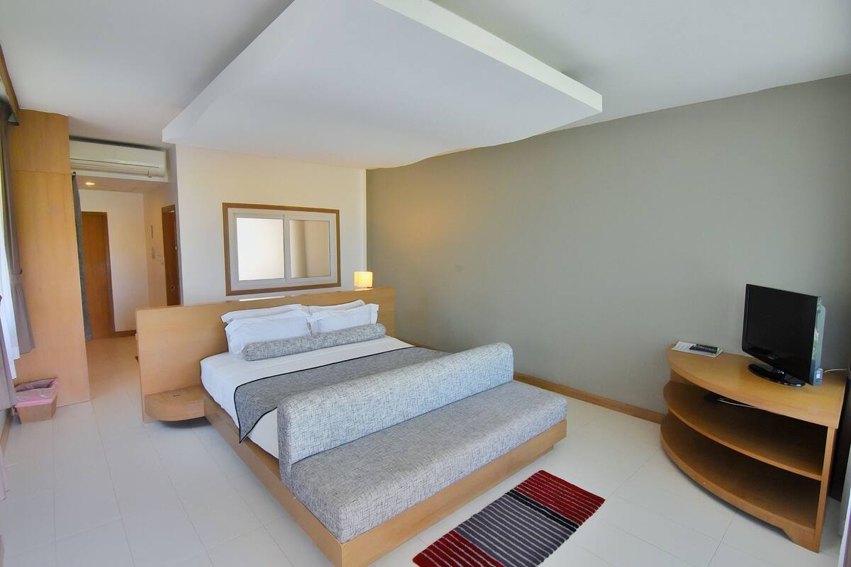 A bedroom with a bed, a television, a mirror, and a small wooden side table.