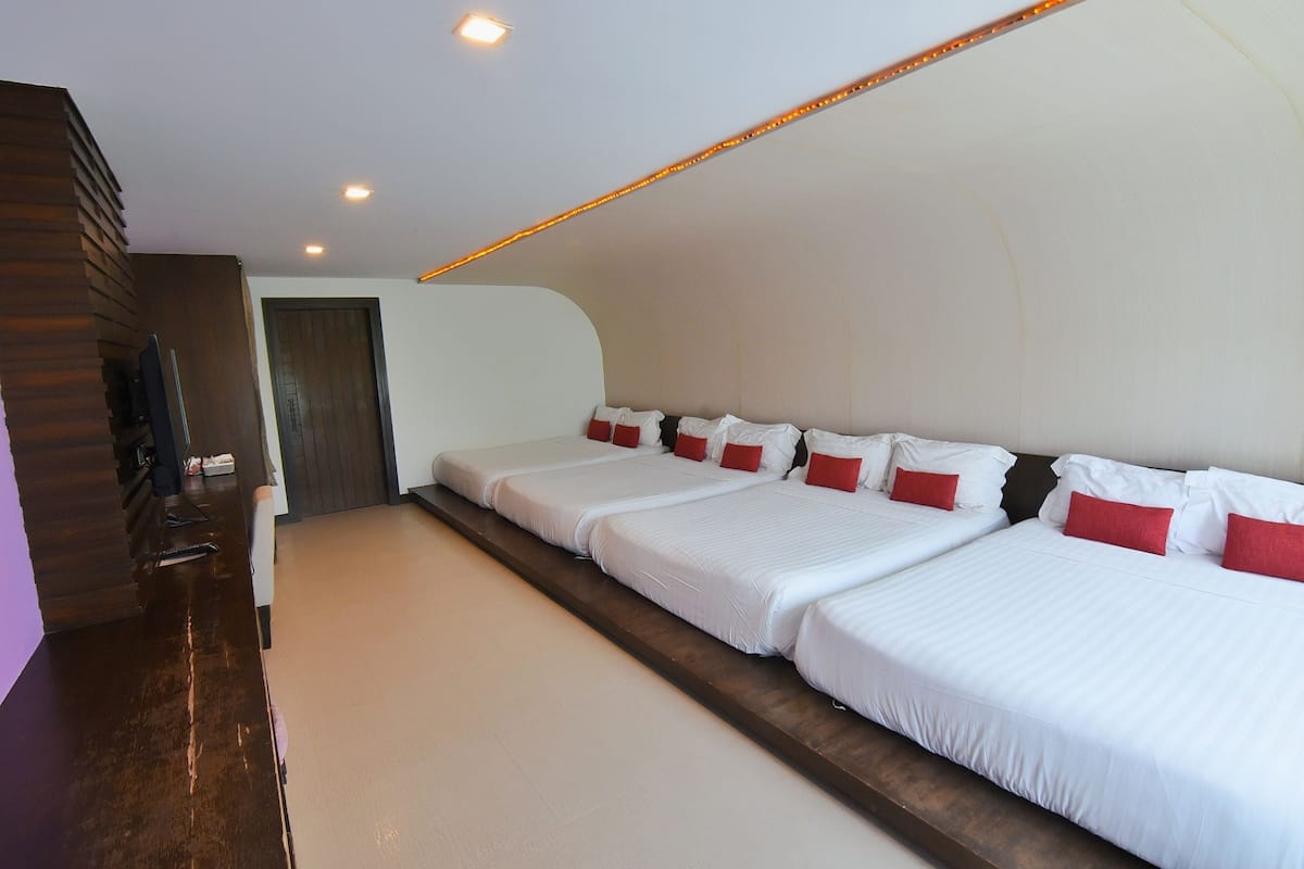 A hotel room with three beds aligned along one wall, a wooden bench, and a television on a stand.