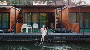 A modern floating house with a covered deck, outdoor seating, and a view of the water. - Suansaiyok Resort (Sai Yok)