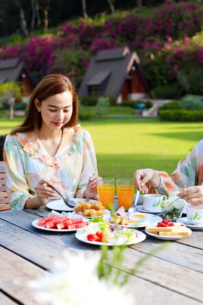 A dining table with various food items and drinks, surrounded by lush greenery and a well-maintained lawn. - Suansaiyok Resort (Sai Yok)