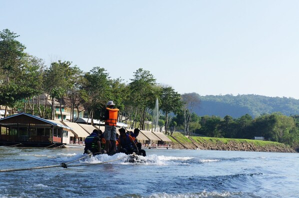 A group of people on a boat with a guide, navigating through a river with buildings and trees in the background.