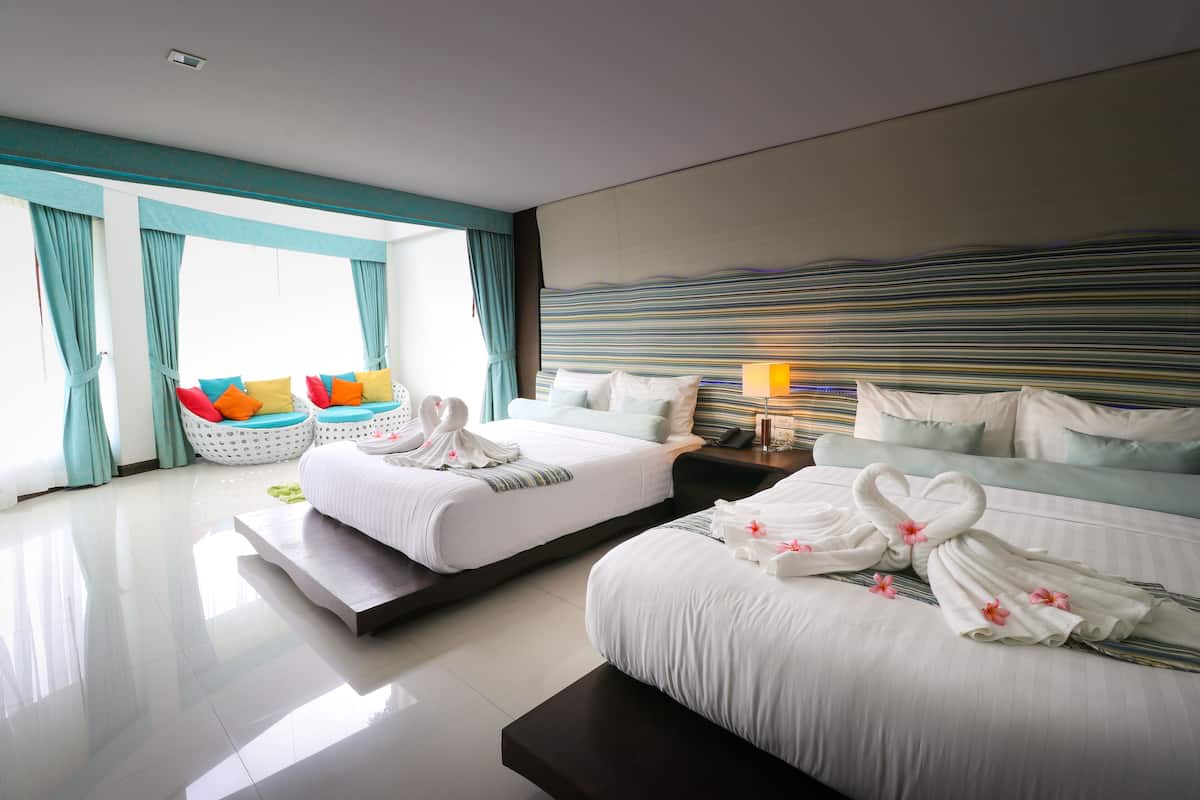 A hotel room with two beds, a large window with curtains, a sofa with cushions, and a headboard with a striped pattern.