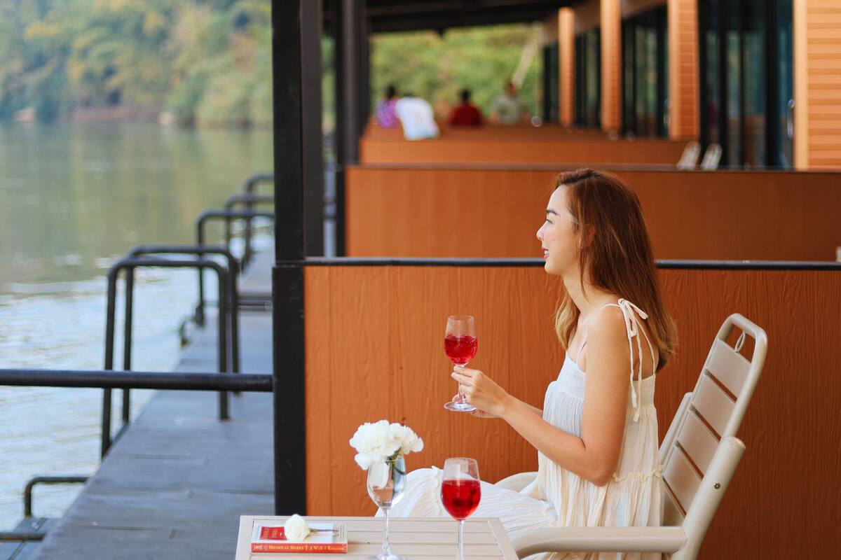 A woman seated at a table by a lake, holding a glass of red wine.