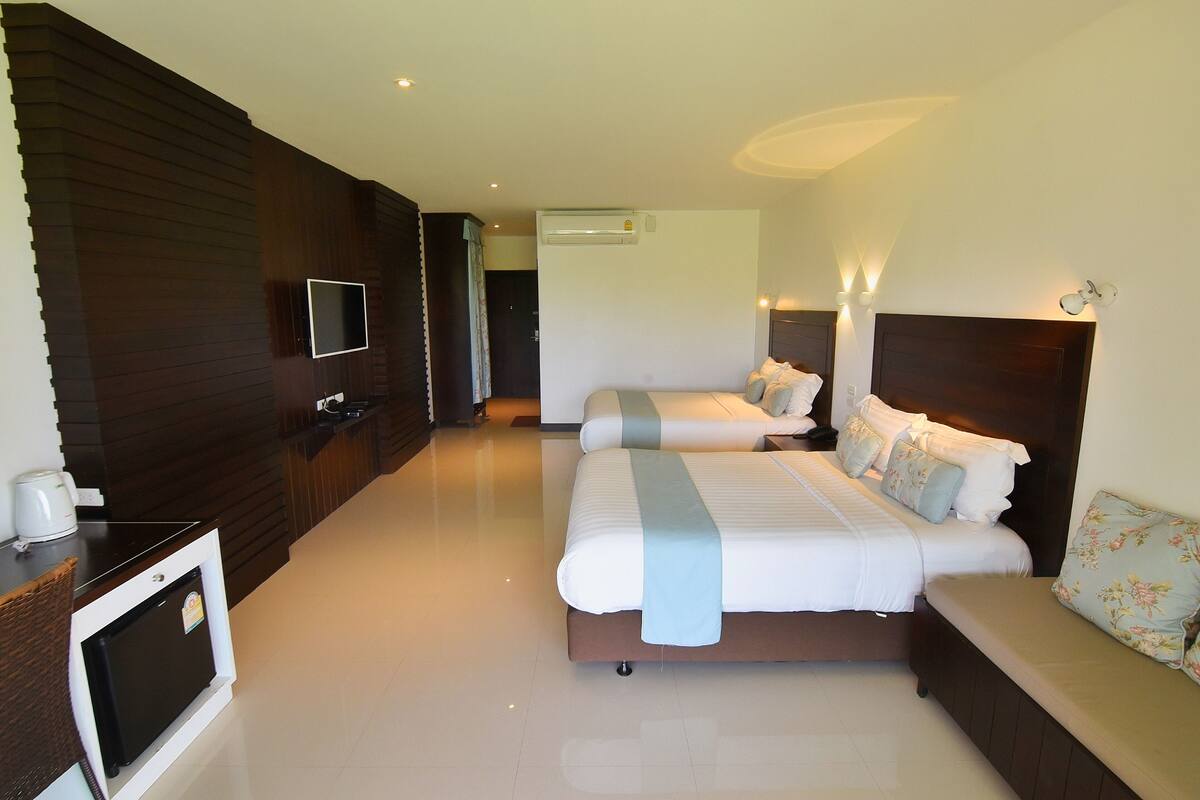 A hotel room with two beds, a TV, a minibar, and a ceiling fan.