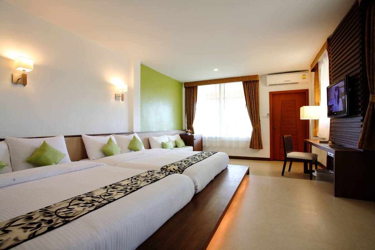 A hotel room with two beds, a desk, a TV, and an air conditioning unit.