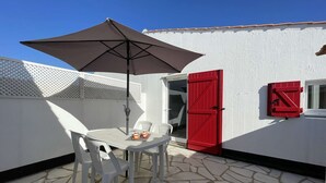 Eine Terrasse im Freien mit Tisch und Stühlen, einer roten Tür und einer weißen Wand.