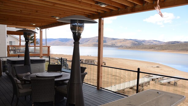Une terrasse couverte, aménagée avec du mobilier d’extérieur, une table et une lampe, qui offre une vue sur un lac et des collines.